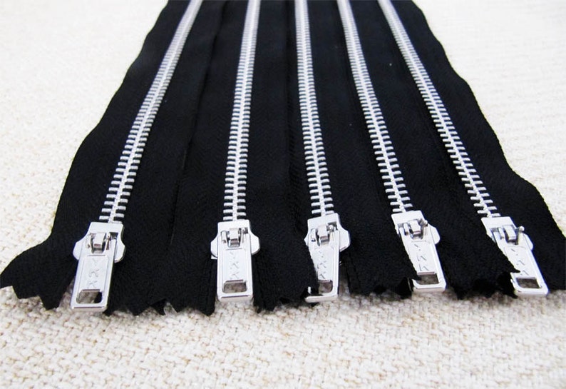 May include: Six silver metal zippers with black tape. The zippers are all closed and have a silver slider.