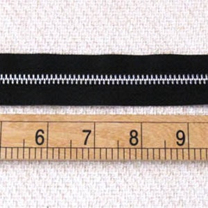 May include: A black zipper measuring 14 inches long, laid out on a wooden ruler with inch markings.