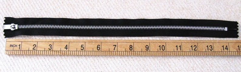 May include: A black zipper measuring 14 inches long, laid out on a wooden ruler with inch markings.