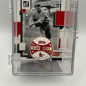 Könnte beinhalten: Eine Baseballkarte in einer transparenten Hülle mit einem Schwarz-Weiß-Bild eines Baseballspielers. Eine Red Sox-Anstecknadel mit "World Series 1918" und "Fenway Park Boston" befindet sich vor der Karte.