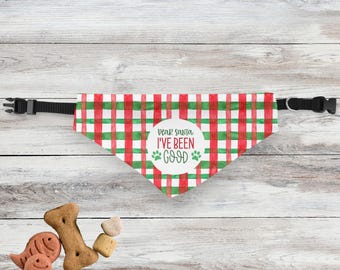 May include: A red, green, and white plaid dog bandana with the text "Dear Santa I've Been Good" in a white circle. The bandana is attached to a black adjustable collar. Several dog treats are scattered below the bandana.