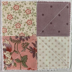 May include: Square patchwork coaster with four fabric squares. The top left square has a cream background with red floral patterns. The top right square is a solid mauve with dark mauve dots. The bottom left square has a pink background with floral patterns. The bottom right square has a cream background with small mauve dots.