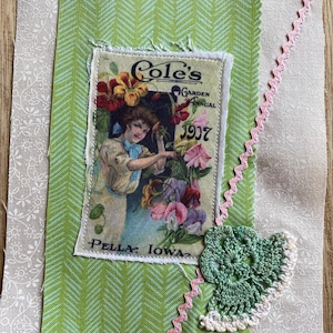 Op de afbeelding: Een stoffen collage met een vintage afbeelding van "Cole's Garden Annual 1907" met een vrouw en bloemen. De collage bevat groen en wit patroonstof, een roze zigzagrand en een groen gehaakt blad.