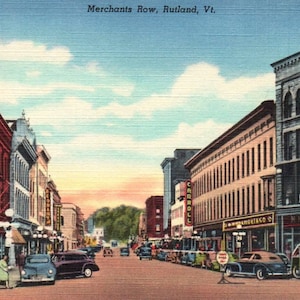 Può includere: Cartolina vintage raffigurante Merchants Row a Rutland, Vermont. La strada è fiancheggiata da edifici, auto e persone. Il cielo è un mix di blu e arancione. Il testo "Merchants Row, Rutland, Vt." è visibile in alto.