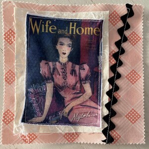 May include: A fabric square featuring a vintage magazine cover with the text "Wife and Home." The cover art depicts a woman in a pink dress. The square is layered with patterned fabrics in pink and cream, and a black zigzag trim.
