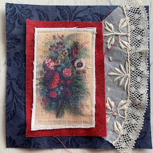 Op de afbeelding: Een stoffen collage met een bloemenprint, omlijst door rode stof en geplaatst tegen een marineblauwe achtergrond met een bladerenpatroon. Een stuk grijze stof met geborduurde bladeren en een kanten rand is bevestigd.