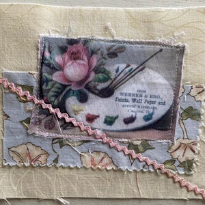 Puede incluir: Un collage de tela con estampado floral y una imagen vintage de una paleta de pintor con pinceles y el texto "WERNER & BRO., Paints, Wall Paper and ARTISTS MATERIALS Canton, O". Una cinta rosa en zigzag acentúa el diseño.