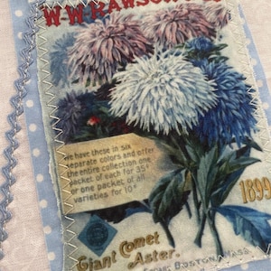 Peut inclure: Un patch en tissu avec une illustration florale vintage de fleurs Giant Comet Aster dans des tons de bleu, violet et blanc. Le patch comprend le texte de W.W. Rawson & Co. et l'année 1899. Le patch est cousu sur un tissu à pois bleu clair.