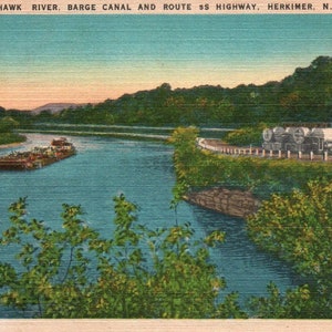 May include: Vintage postcard featuring the Mohawk River, Barge Canal, and Route 5S Highway in Herkimer, NY. The image shows a barge on the river, a highway, and a building with a red roof. The sky is a gradient of blue and orange.