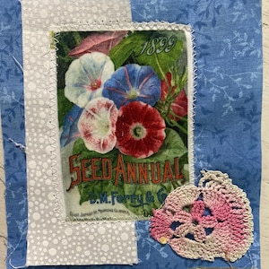 May include: A fabric square featuring a blue floral print background, a central rectangular patch with a vintage 1899 Seed Annual illustration of morning glory flowers, and a small pink and white crocheted lace flower appliqué in the corner.