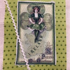 May include: A St. Patrick's Day greeting card featuring a vintage illustration of a woman in a green dress standing on a map of Ireland, surrounded by a shamrock. The card is set on a green patterned fabric with a white lace trim.