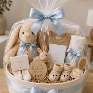 Pu&ograve; includere: Un cesto regalo avvolto in plastica trasparente con un nastro azzurro contenente un coniglietto di peluche beige, un sonaglio a forma di coniglio all'uncinetto, un body beige, una coperta bianca a fiori, calzini, scarpine a orsetto e una spazzola.