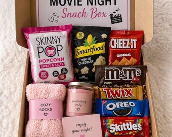 Può includere: Una scatola di snack per una serata al cinema accogliente, piena di popcorn, cracker, caramelle e altre prelibatezze. Include una candela rosa, calzini morbidi e un biglietto con la scritta "enjoy your night!" La scatola è decorata con cuori.