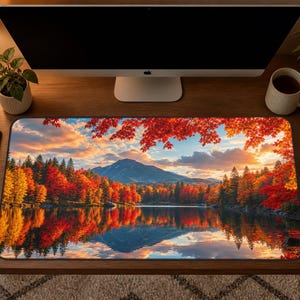 May include: A rectangular desk mat featuring a vibrant autumn landscape print. The image displays a calm lake reflecting a mountain range and a dense forest with bright red, orange, and yellow foliage under a sunset sky with soft clouds.