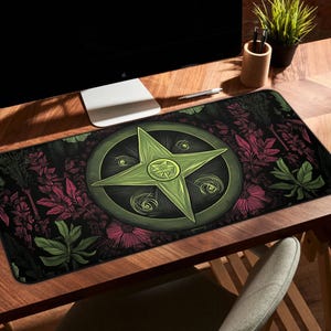 May include: A rectangular desk mat featuring a central green star design within a circular frame. The mat has a black background with a pattern of green leaves and pink flowers. The mat is placed on a wooden desk.