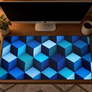 May include: A rectangular desk mat featuring a repeating geometric pattern of three-dimensional cubes in various shades of blue, ranging from dark navy to bright cyan, creating an optical illusion of depth across the entire surface of the mat.