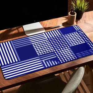 May include: A blue and white patterned desk mat with a geometric design. The mat features a combination of stripes, dots, and squares. The mat is rectangular and designed to protect a desk surface.