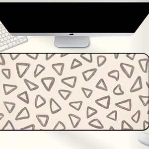 May include: A rectangular desk mat with a beige background and a pattern of gray, outlined triangles. The mat is positioned under a computer monitor, keyboard, and mouse, suggesting a workspace setup.