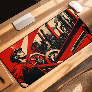 May include: A rectangular desk mat featuring a graphic illustration in red, black, and cream. The design depicts a worker in a cap looking upward toward a large industrial factory complex with tall smokestacks, pipes, and prominent mechanical gears.