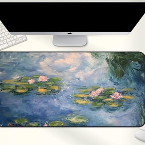 May include: A rectangular desk mat featuring a water lily pond scene with pink flowers and green lily pads. The artwork is in a painterly style with blue, green, and white hues. A computer, keyboard, and mouse are visible.