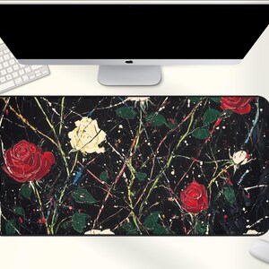 May include: A rectangular black mouse pad featuring a floral design with red and white roses, green leaves, and white paint splatters. The pad is placed under a computer monitor, keyboard, and mouse.