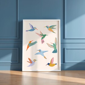 Op de afbeelding: Een rechthoekige wandkunstprint met acht gestileerde kolibries in verschillende vliegposities. De vogels zijn weergegeven in levendige kleuren, waaronder blauw, groen, oranje, roze en geel, tegen een effen, lichtcr&egrave;mekleurige achtergrond.