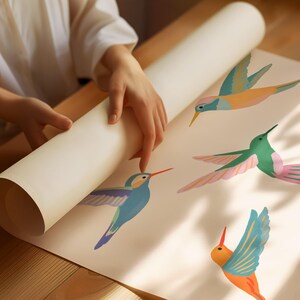 Op de afbeelding: Een rol gebroken wit papier met een herhalend patroon van vier kleurrijke kolibries in vlucht. De vogels zijn afgebeeld in tinten blauw, oranje, groen en roze met spitse snavels en uitgestrekte vleugels tegen een effen achtergrond.