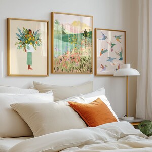Op de afbeelding: Drie ingelijste wandkunstwerken in gouden lijsten. De linker print toont een persoon die een grote bos bloemen vasthoudt. De middelste print toont een landschap met heuvels en wilde bloemen. De rechter print bevat diverse kleurrijke kolibries.