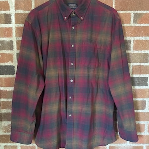 May include: A long-sleeved button-down shirt with a plaid pattern in shades of red, brown, and navy blue. The shirt has a button-down collar and a chest pocket. The brand name "Pendleton" is visible on the label.