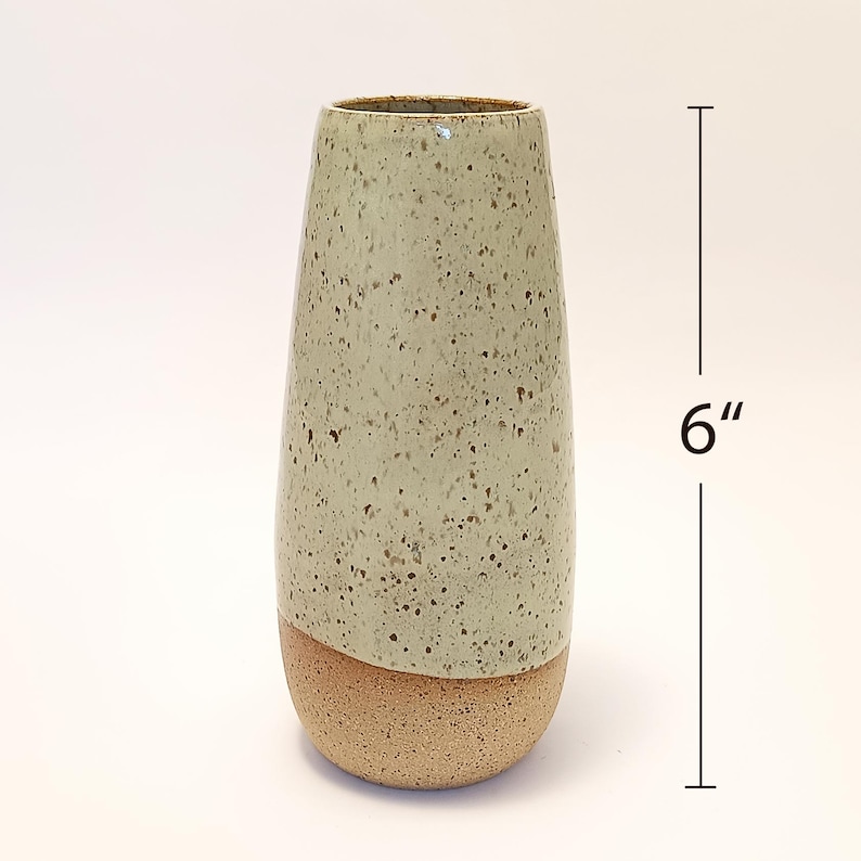 K&ouml;nnte beinhalten: Eine gesprenkelte Keramikvase, etwa 15 cm hoch, mit einem hellgr&uuml;nen oberen Teil und einem beigefarbenen Sockel. Die Vase hat eine leicht konische Form und eine strukturierte Oberfl&auml;che, geeignet f&uuml;r Blumen oder als dekoratives Element.