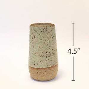 K&ouml;nnte beinhalten: Eine gesprenkelte Keramikvase, ca. 11,4 cm hoch, mit einem hellgr&uuml;nen oberen Teil und einem beigen Sockel. Die Vase hat eine leicht konische Form und eine strukturierte Oberfl&auml;che, geeignet f&uuml;r die Inneneinrichtung.