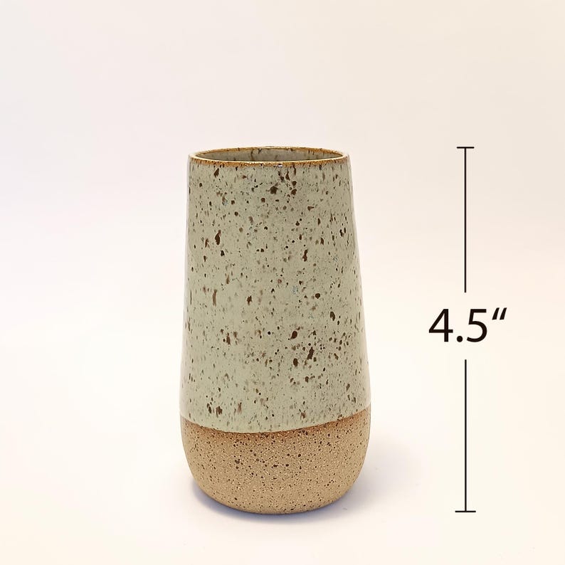 K&ouml;nnte beinhalten: Eine gesprenkelte Keramikvase, ca. 11,4 cm hoch, mit einem hellgr&uuml;nen oberen Teil und einem beigen Sockel. Die Vase hat eine leicht konische Form und eine strukturierte Oberfl&auml;che, geeignet f&uuml;r die Inneneinrichtung.