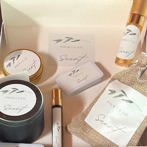 May include: A set of home fragrance products with a natural, earthy theme. The set includes a candle, a small bottle of essential oil, a sachet, and a small tin of scented wax. The labels on the products feature a simple design with the text "Pour La Vie Scent".