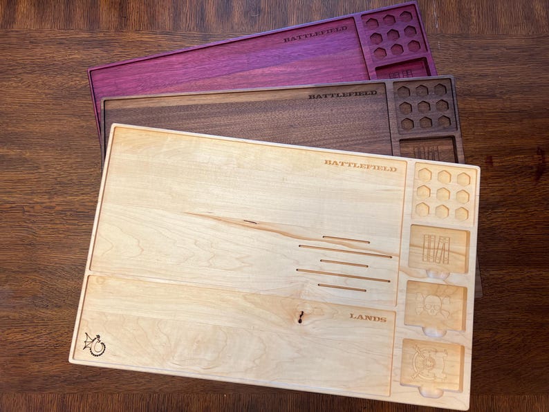 May include: Three wooden game trays in shades of purple, brown, and light wood. Each tray is rectangular with carved compartments and the word "BATTLEFIELD" etched across the top. The light wood tray has the word "LANDS" etched on it.