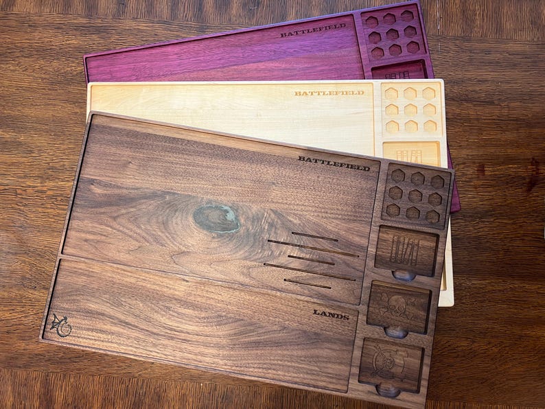 May include: Three wooden game trays in shades of brown, cream, and purple. Each tray has compartments and the word "BATTLEFIELD" engraved on it. The bottom tray also has the word "LANDS" engraved.