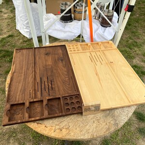 May include: Two wooden game boards, one dark brown and one light brown, are displayed. The dark brown board has carved slots and images, while the light brown board has etched lines. Both boards are rectangular and sit on a round wooden table.