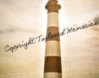 May include: A tall lighthouse with black and white stripes stands against a cloudy sky. A small white building with a dark roof sits at the base of the lighthouse. The words "Copyright Taylored Memories" are written across the image.