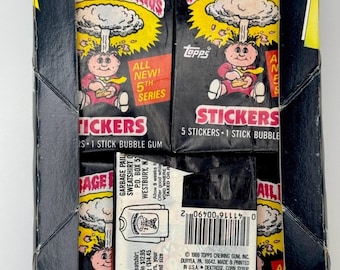 May include: A box of Garbage Pail Kids stickers with a black background and a cartoon character on the front. The box says "All New! 5th Series" and "5 Stickers - 1 Stick Bubble Gum".