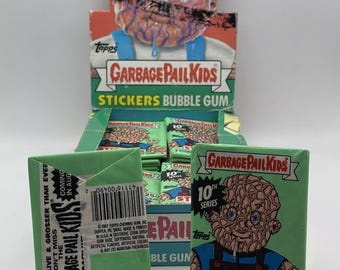 May include: A pack of Garbage Pail Kids stickers and bubble gum. The pack is green and features a cartoon character with a green face and a blue shirt. The text on the pack reads "Garbage Pail Kids 10th Series Stickers 5 Stickers - 1 Stick Bubble Gum".