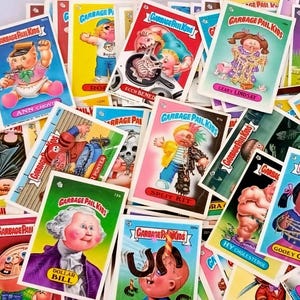 May include: A collection of Garbage Pail Kids trading cards. The cards feature colorful, cartoonish illustrations of grotesque characters with humorous names. The cards are scattered, showcasing various designs and titles like "Ann Chovy" and "Leaky Lindsay".
