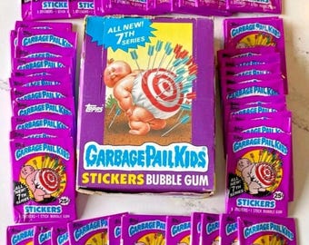 May include: A collection of Garbage Pail Kids stickers and bubble gum packs. The packaging is primarily purple with the Garbage Pail Kids logo and character illustrations. The box reads "All New! 7th Series".