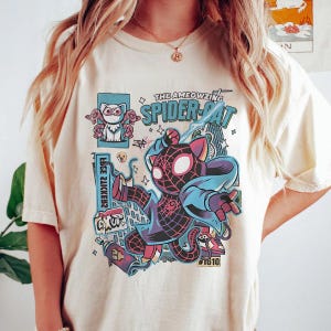 Puede incluir: Camiseta color crema con un gr&aacute;fico colorido de un gato con un disfraz inspirado en Spider-Man. El dise&ntilde;o incluye el texto "THE AMEOWZING SPIDER-CAT" y otros elementos de dibujos animados. Es una prenda informal.