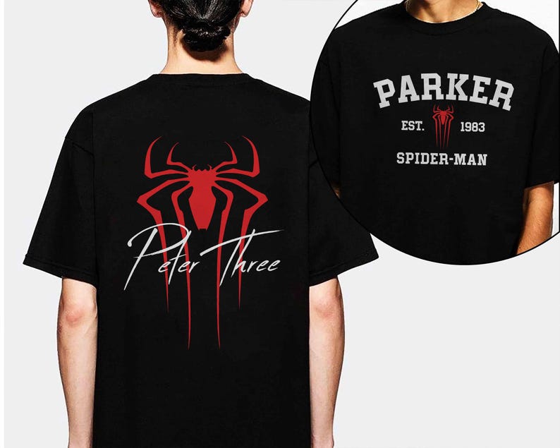 May include: Black t-shirt featuring a red spider-like emblem and the words "Peter Three" in white script. A smaller image shows the front of the shirt with "Parker" above "Spider-Man" and the year "1983".
