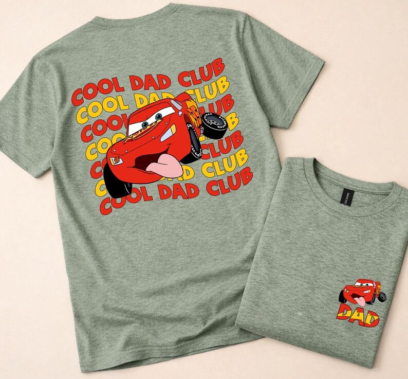 May include: Two heather green t-shirts. One features a red cartoon race car graphic with the text "COOL DAD CLUB" in yellow and red. The other shirt has a smaller car graphic with the word "DAD".