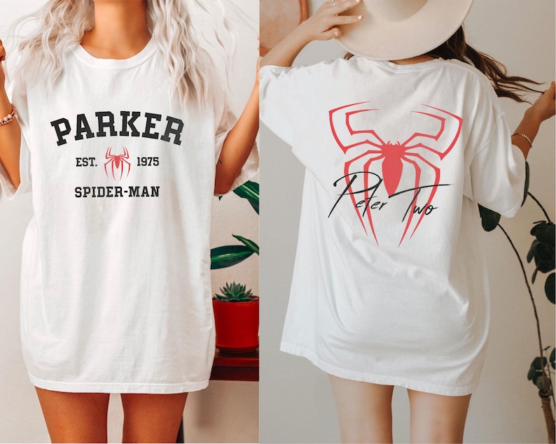 May include: White t-shirt featuring the text "PARKER EST. 1975 SPIDER-MAN" in black and red. The back of the shirt displays a red spider graphic with the text "Peter Two" in black script. The shirt is a casual, oversized fit.