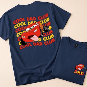 May include: Two navy blue t-shirts. One features a large graphic of a red cartoon race car with the text "COOL DAD CLUB" in yellow and red. The other shirt has a smaller version of the car and the word "DAD".