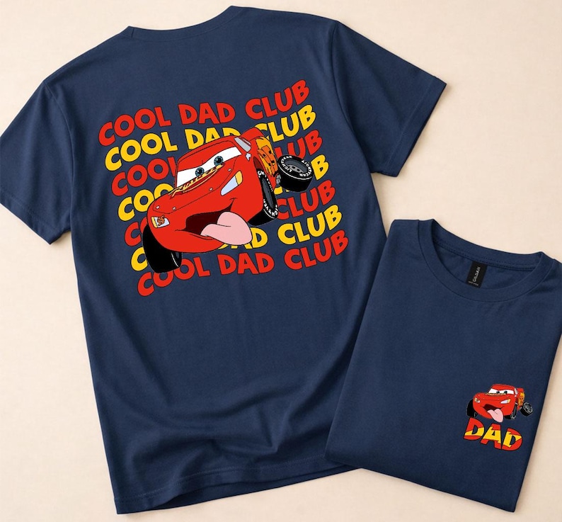 May include: Two navy blue t-shirts. One features a large graphic of a red cartoon race car with the text "COOL DAD CLUB" in yellow and red. The other shirt has a smaller version of the car and the word "DAD".