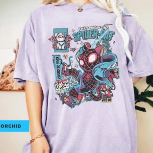 Puede incluir: Camiseta color orqu&iacute;dea con un gr&aacute;fico de "The AMEOWZING SPIDER-CAT". El dise&ntilde;o presenta un personaje de Spider-Man felino en acci&oacute;n, con elementos de la ciudad y texto. La camiseta tiene un corte holgado.