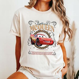 Puede incluir: Una camiseta beige con un dise&ntilde;o de Rayo McQueen de la pel&iacute;cula Cars. El dise&ntilde;o incluye el texto "Lightning McQueen" y una imagen estilizada del coche de carreras rojo. La camiseta tiene mangas cortas.