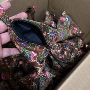 May include: A box filled with brown fabric pouches with a colorful floral pattern. The pouches have a zipper closure and are lined with black fabric.